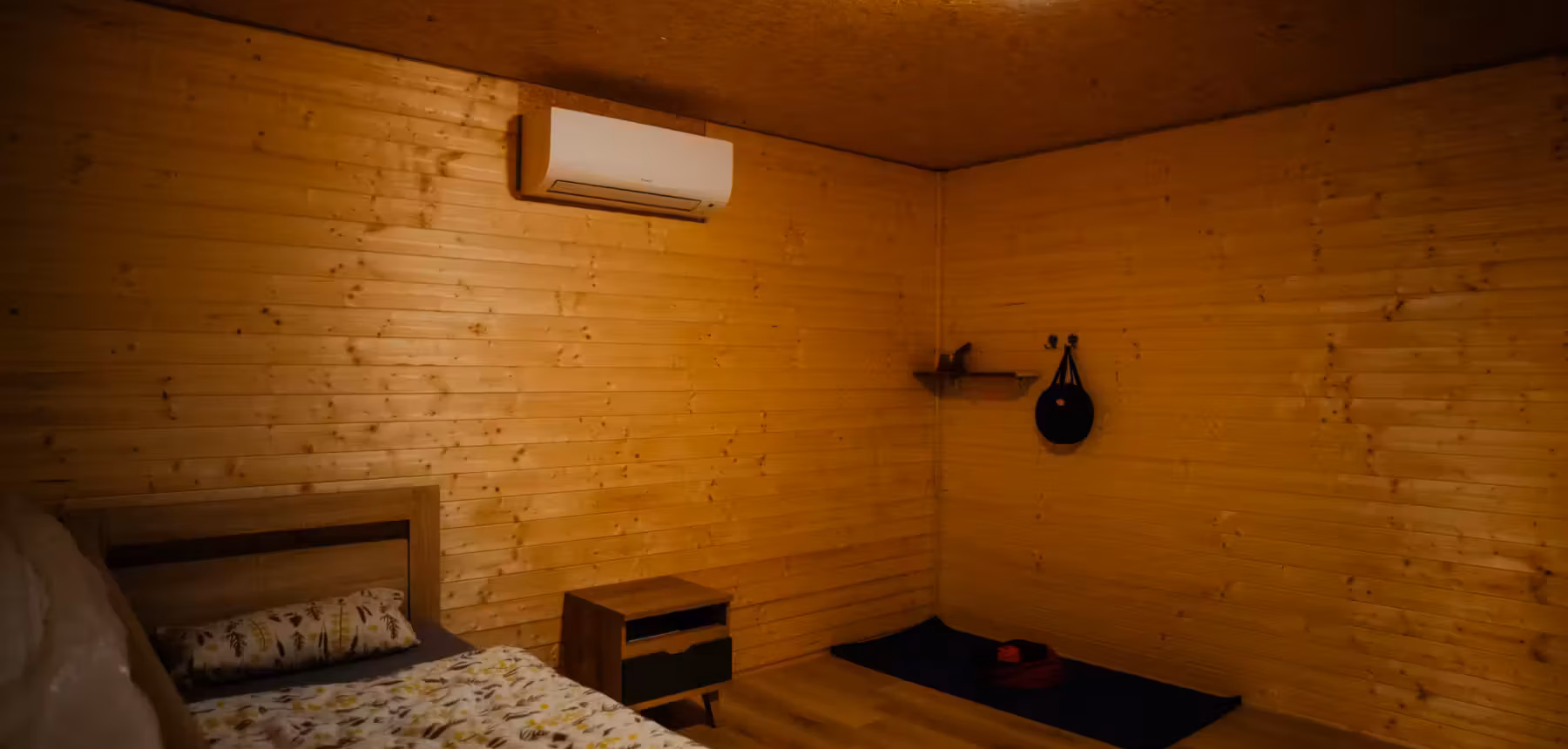 Inside a dark retreat cabin: bed, mat and shelf, lights on