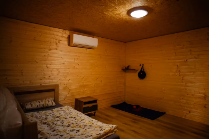 Inside a dark retreat cabin: bed, mat and shelf, lights on